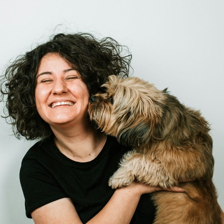 Lächelnde Person mit lockigem Haar, die einen Hund im Arm hat.